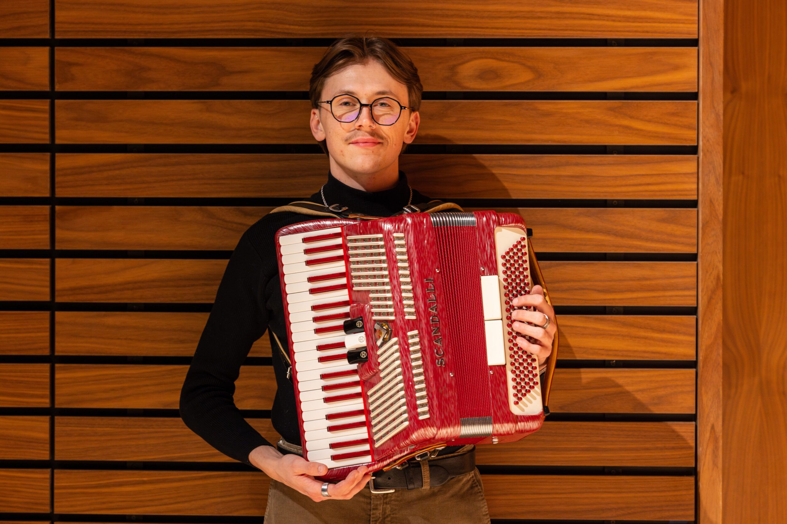 Will Whitten poses for a portrait with an accordion musical instrument.