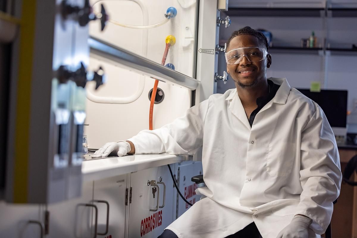 An NAU Health Sciences student smiles and poses while wearing their lab coat and protective goggles.