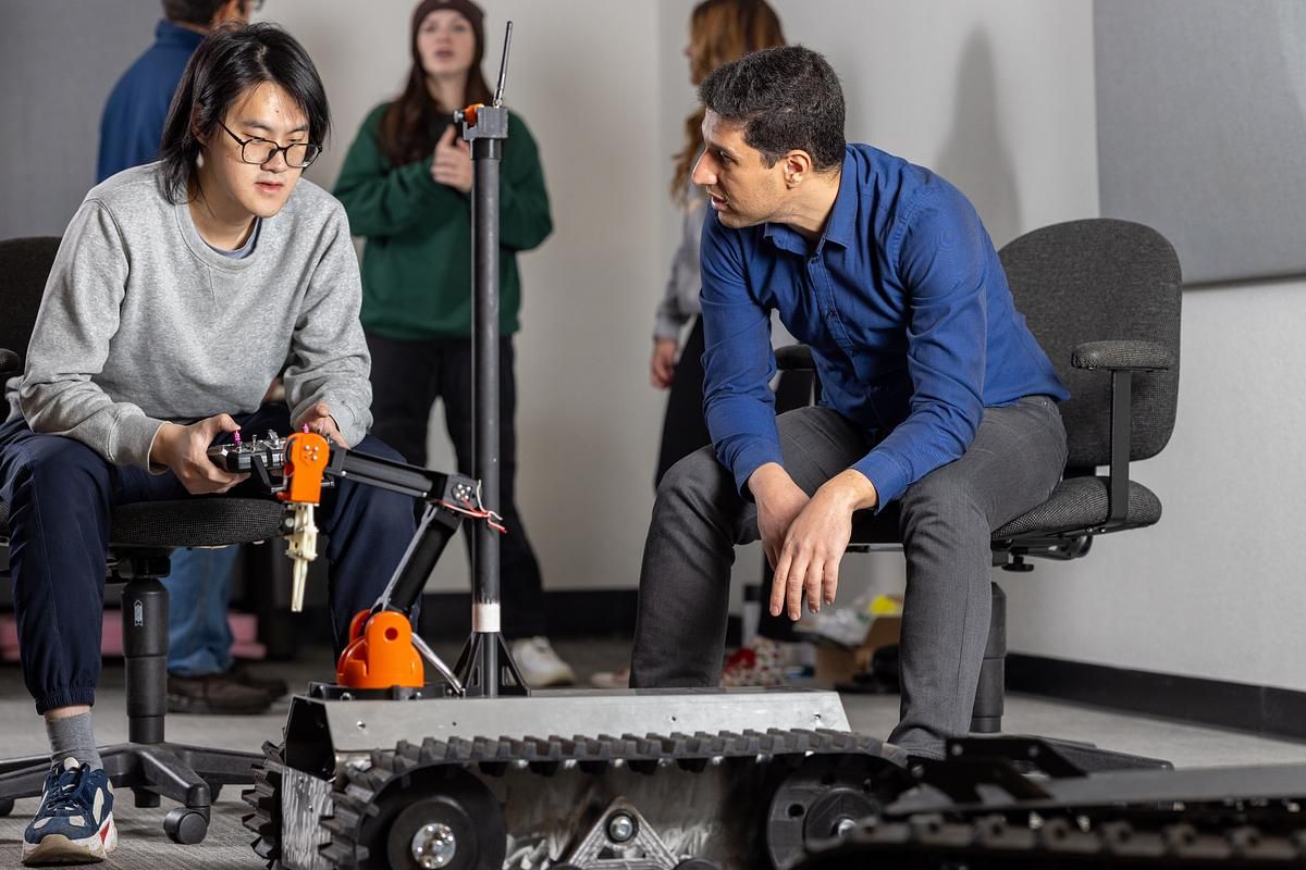 A student and professor in the N A U engineering lab control a robot with a remote control.
