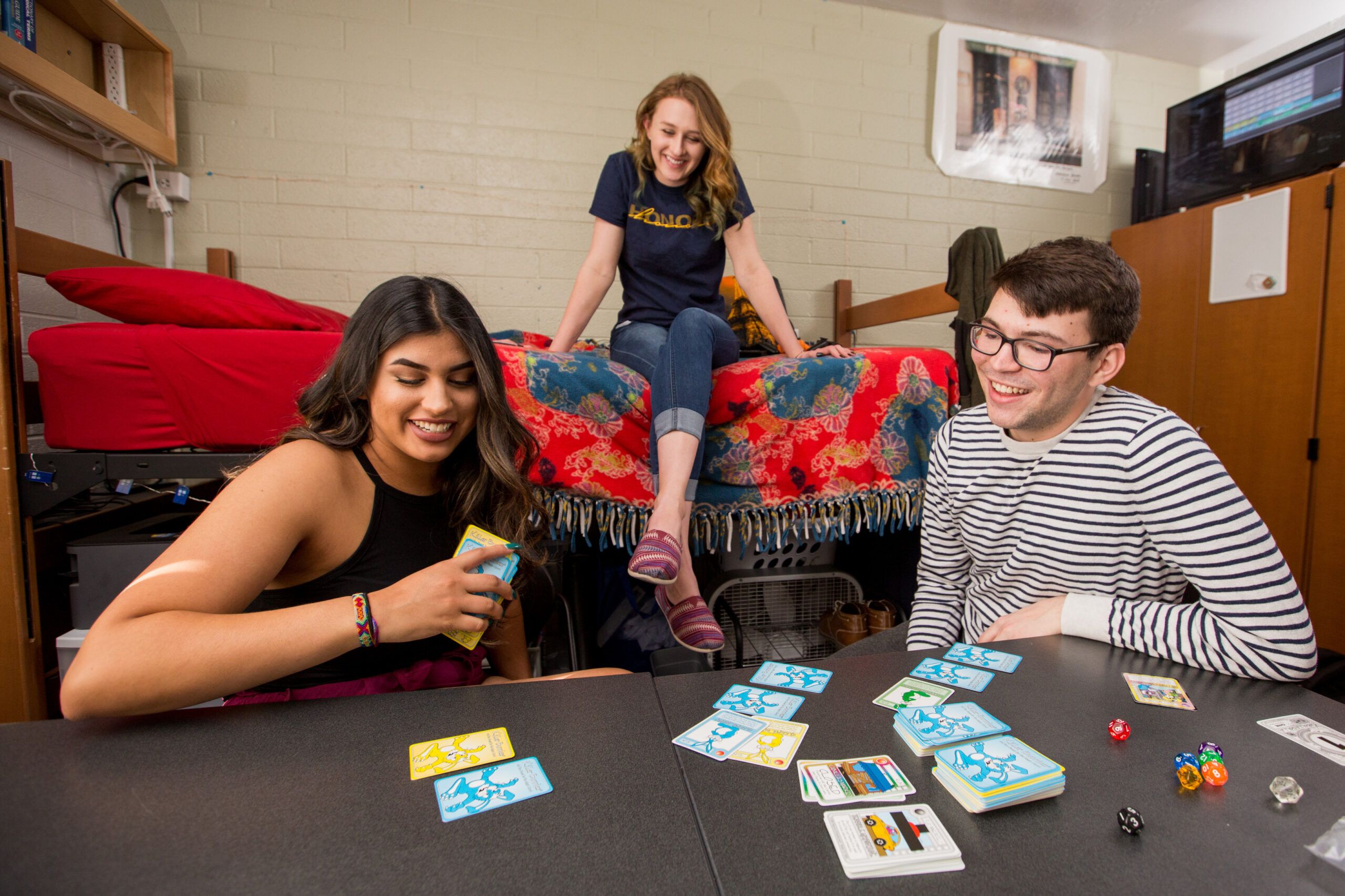 Three students playing cards in a dorm room.