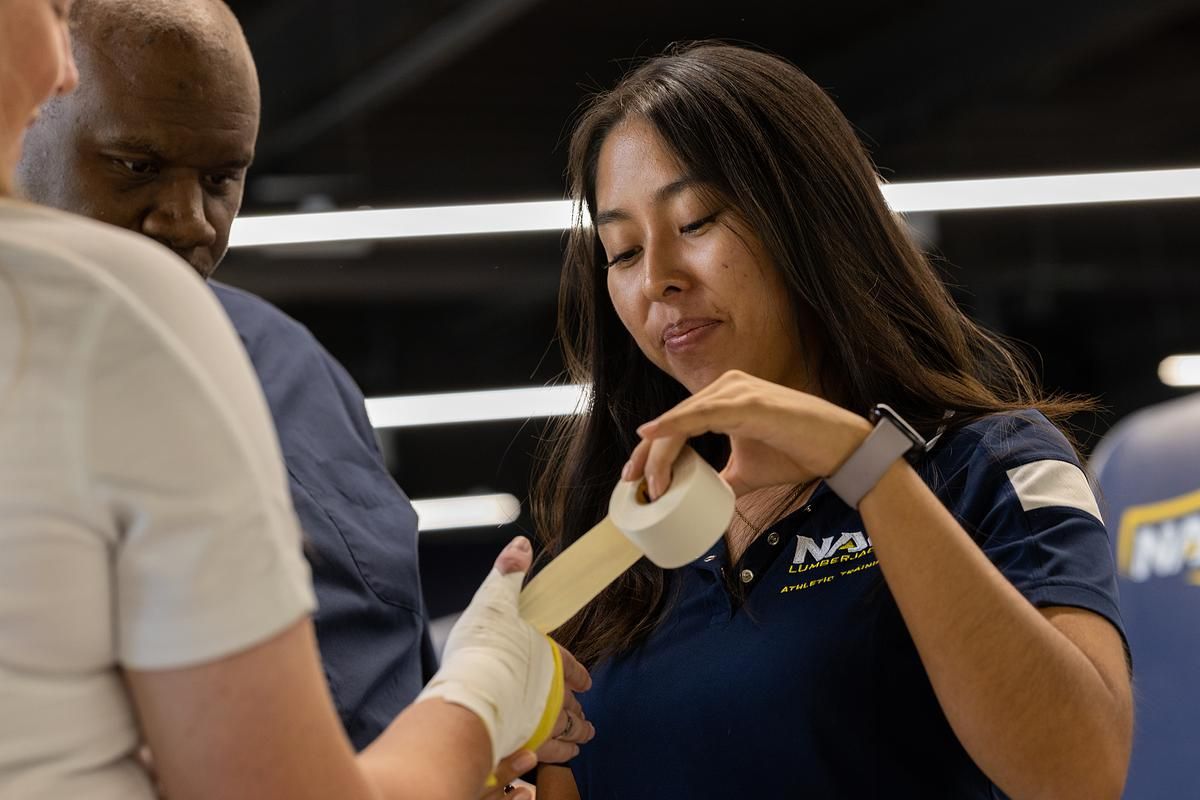 A student and professor bandages an athletes hand.