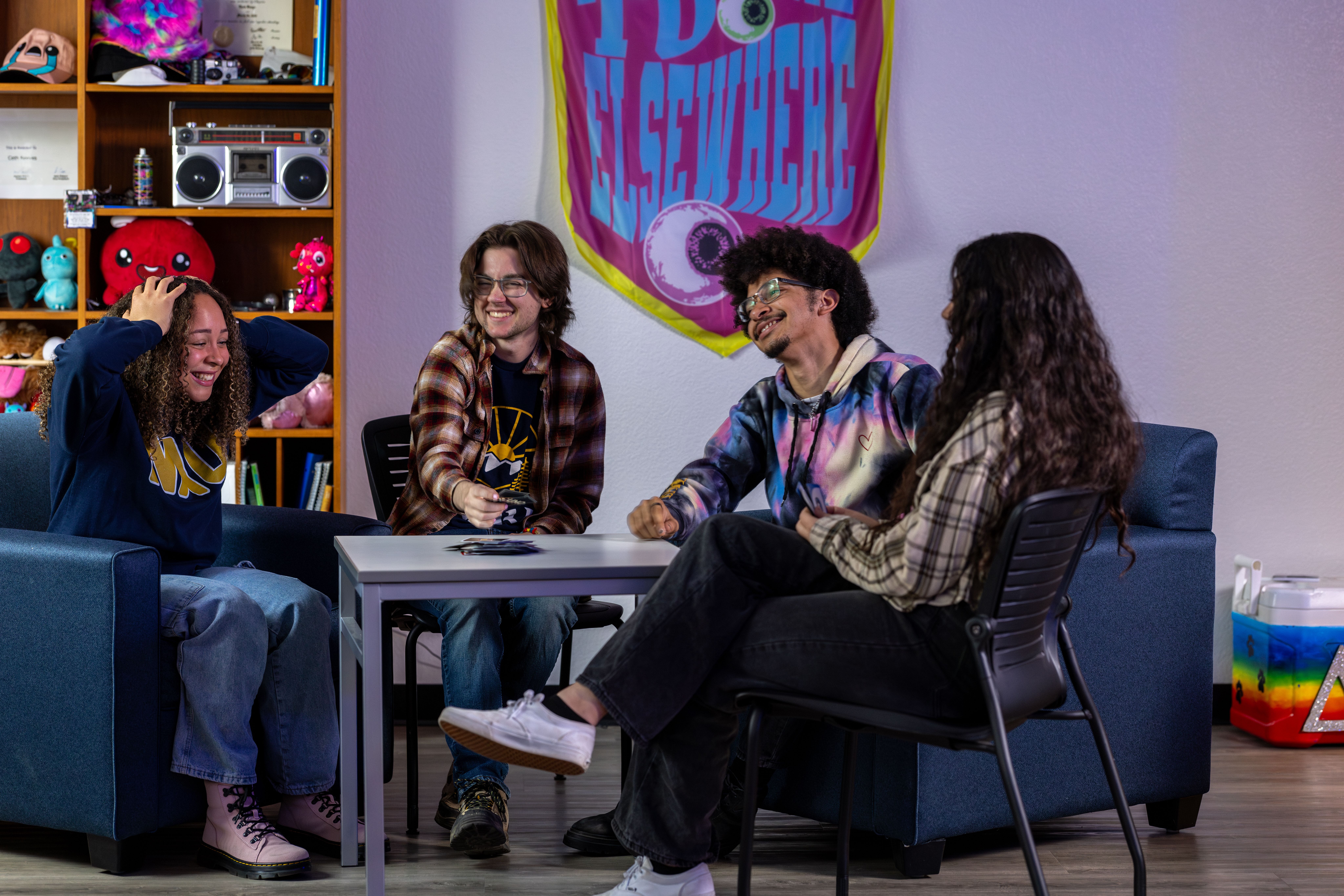 Four students play games and hang out in a res life dorm room.