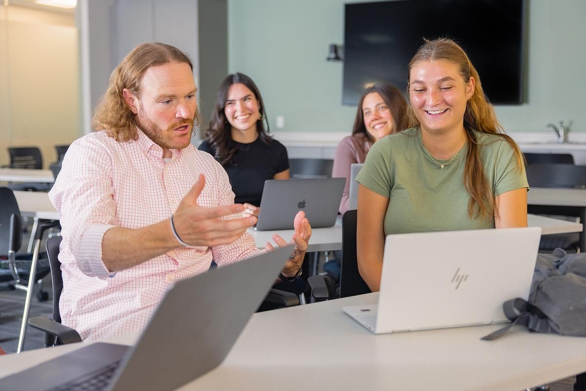 Professor sits with students and discusses psychology in front of laptop.