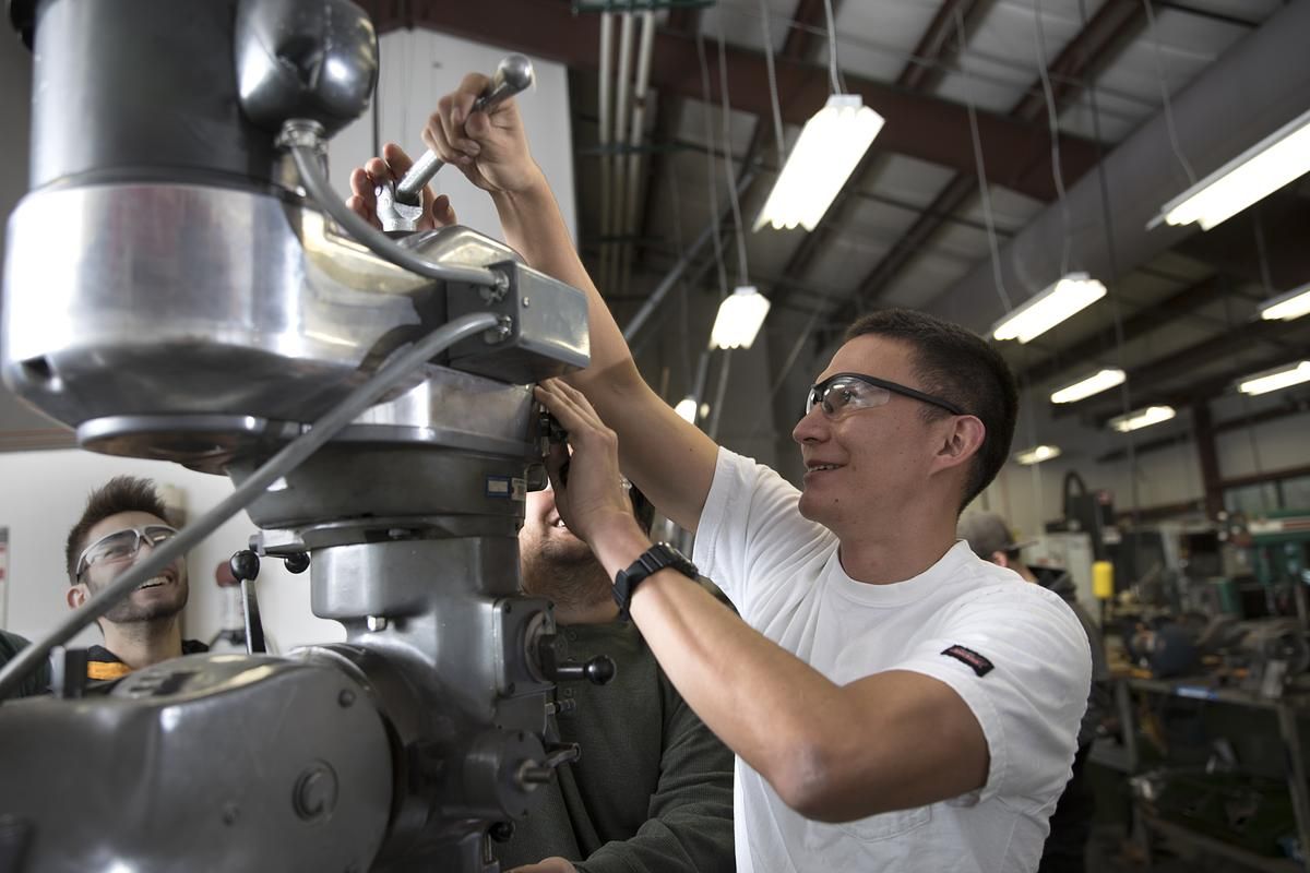 A student wears protective goggles and works with mechanical engineering equipment.