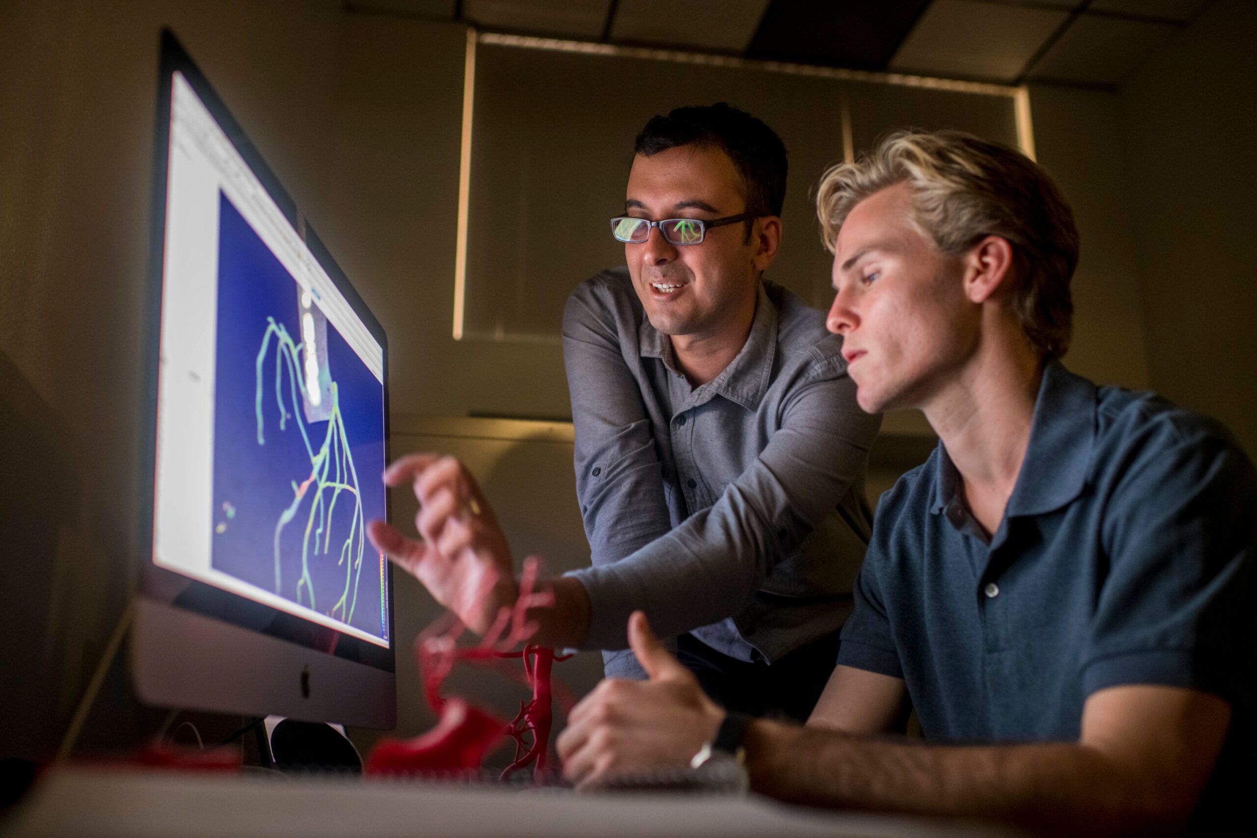Students look over a computer screen with a professor.