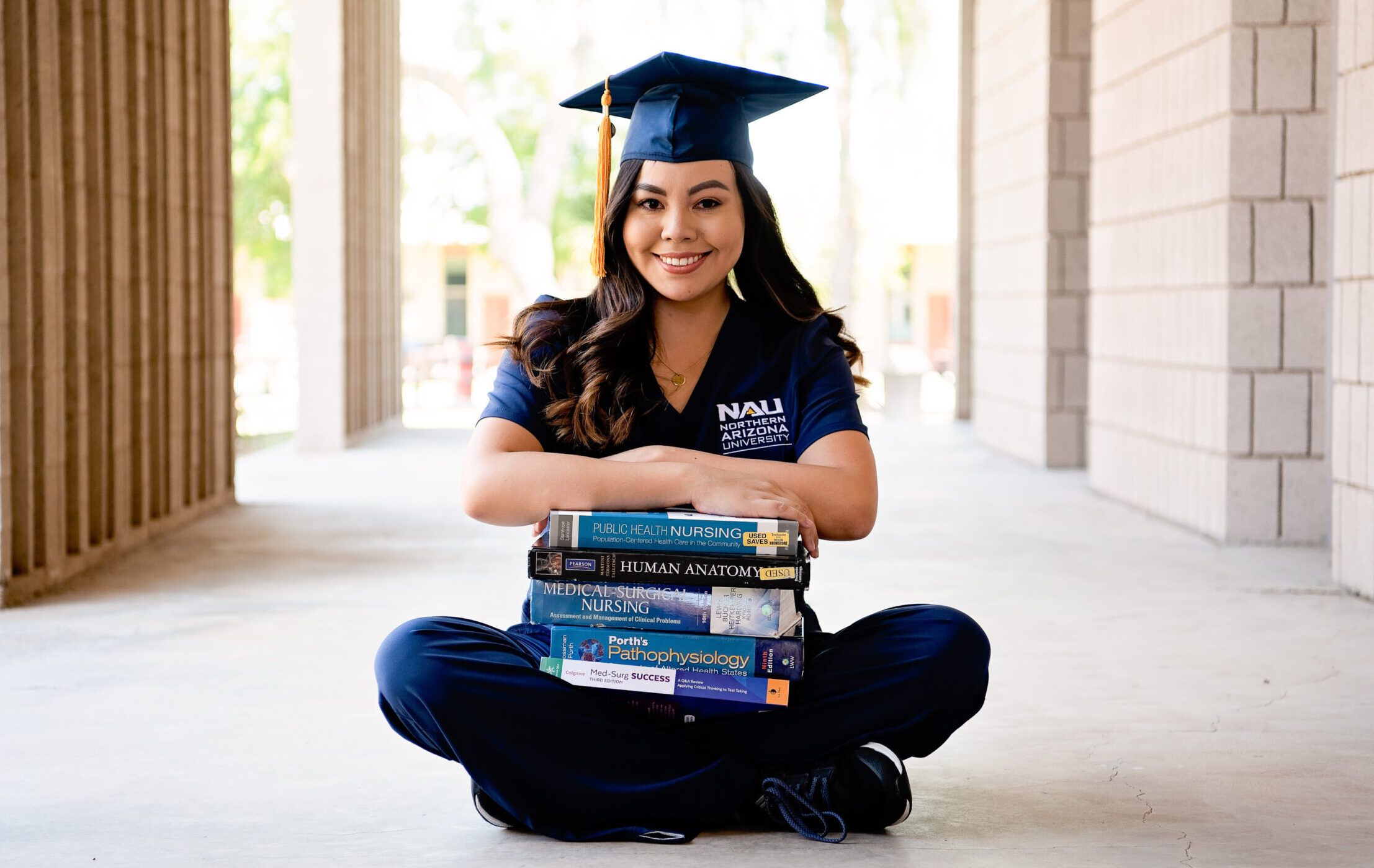 A nursing student holds books while wearing a graduation cap.