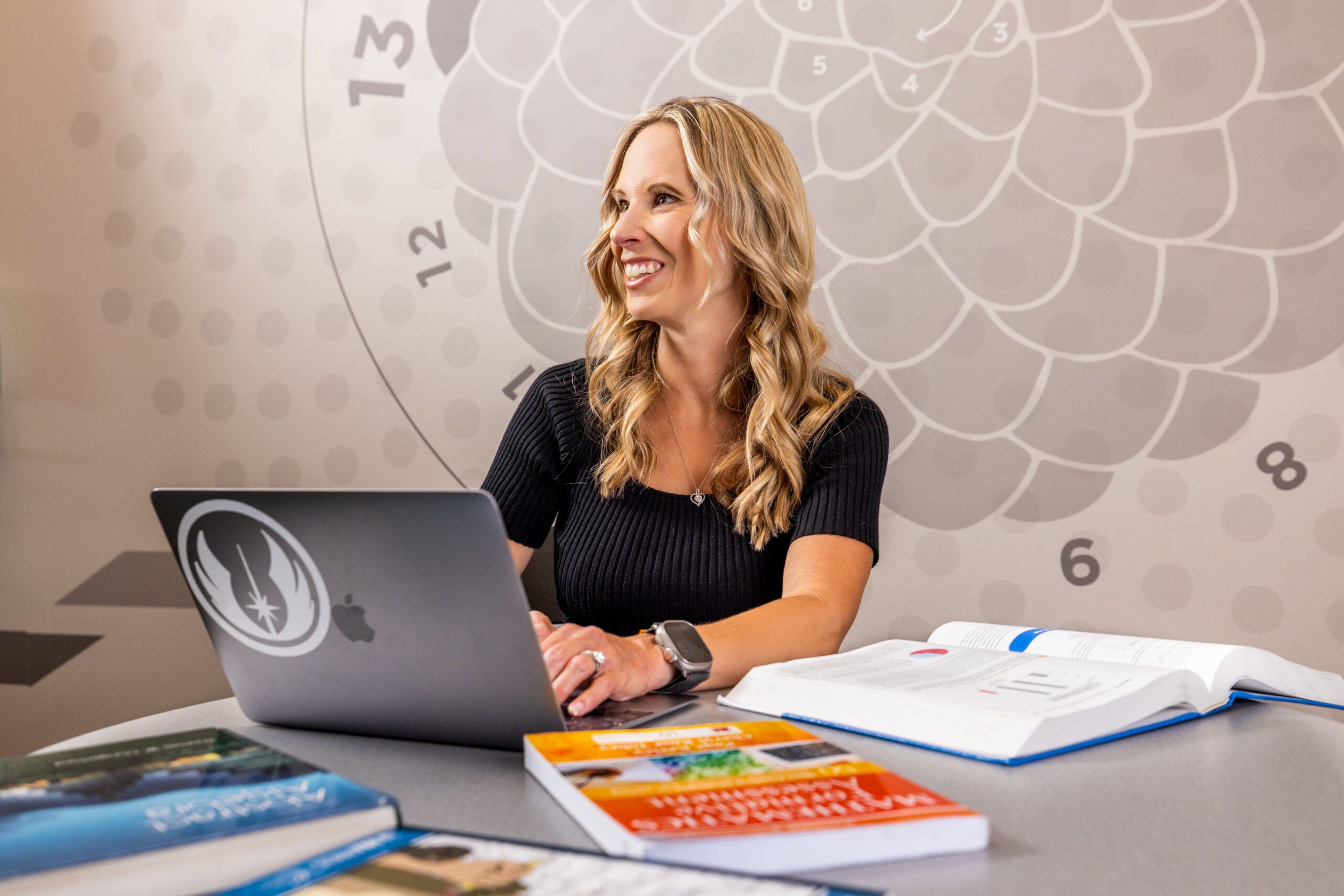 NAU faculty Angie Hodge Zickerman works on a laptop, surrounded by textbooks.