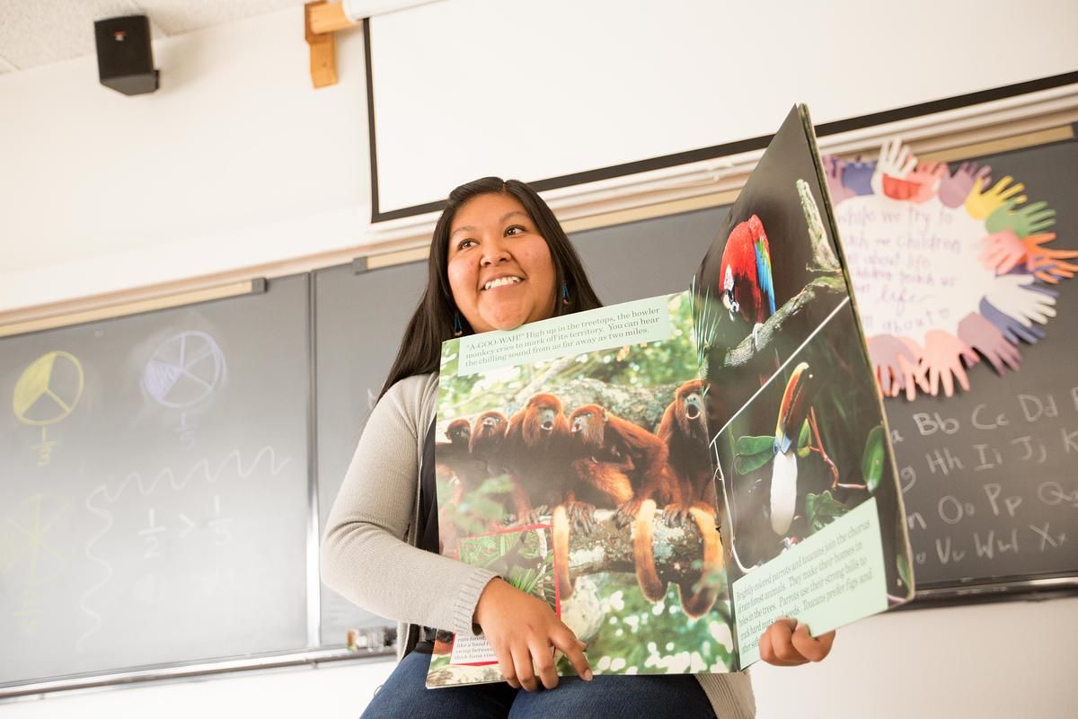 A teacher pointing to parts of a large book on Biology in front of the classroom.