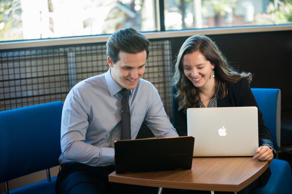 A man and woman sitting at a desk working on computers.