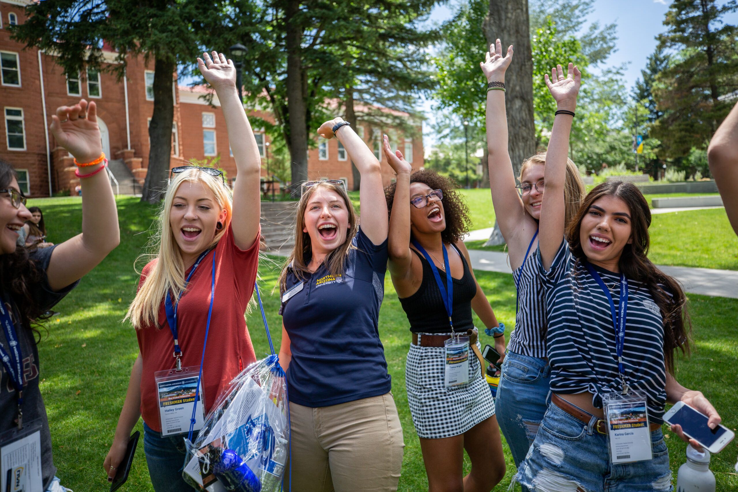 A group of new students excitedly raising their hands in front of Old Main at the NAU Flagstaff campus.