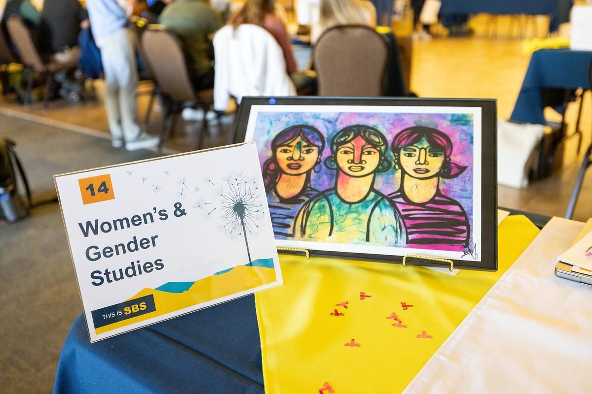 A sign saying Women's and Gender Studies stands next to a small colorful painting of three women.