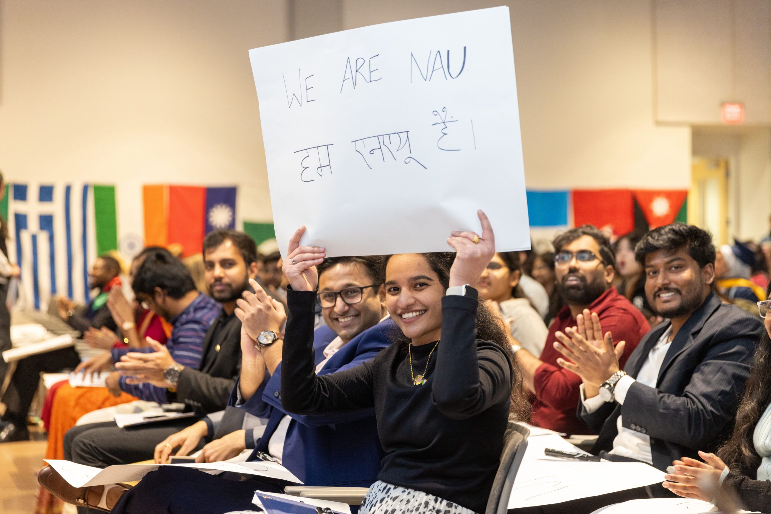 NAU international students smile while holding a sign that says "We are NAU" in both English and Hindi.