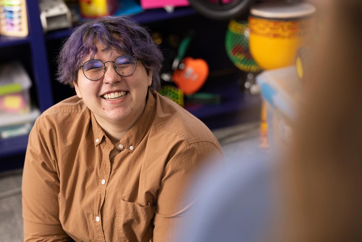 A student teacher sits on the floor of a classroom and smiles for the camera.