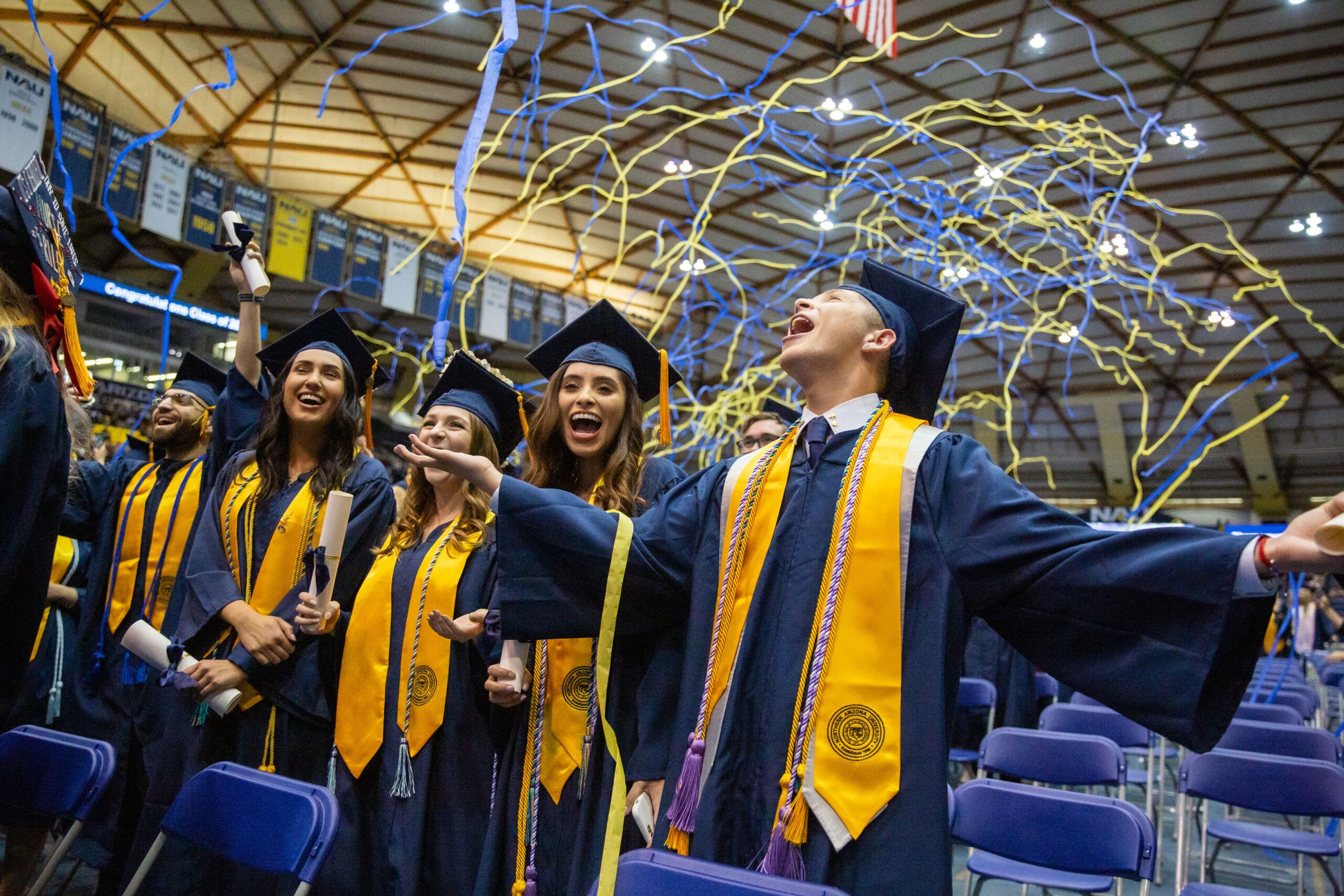 NAU graduating students celebrate at commencement while streamers fall from above.