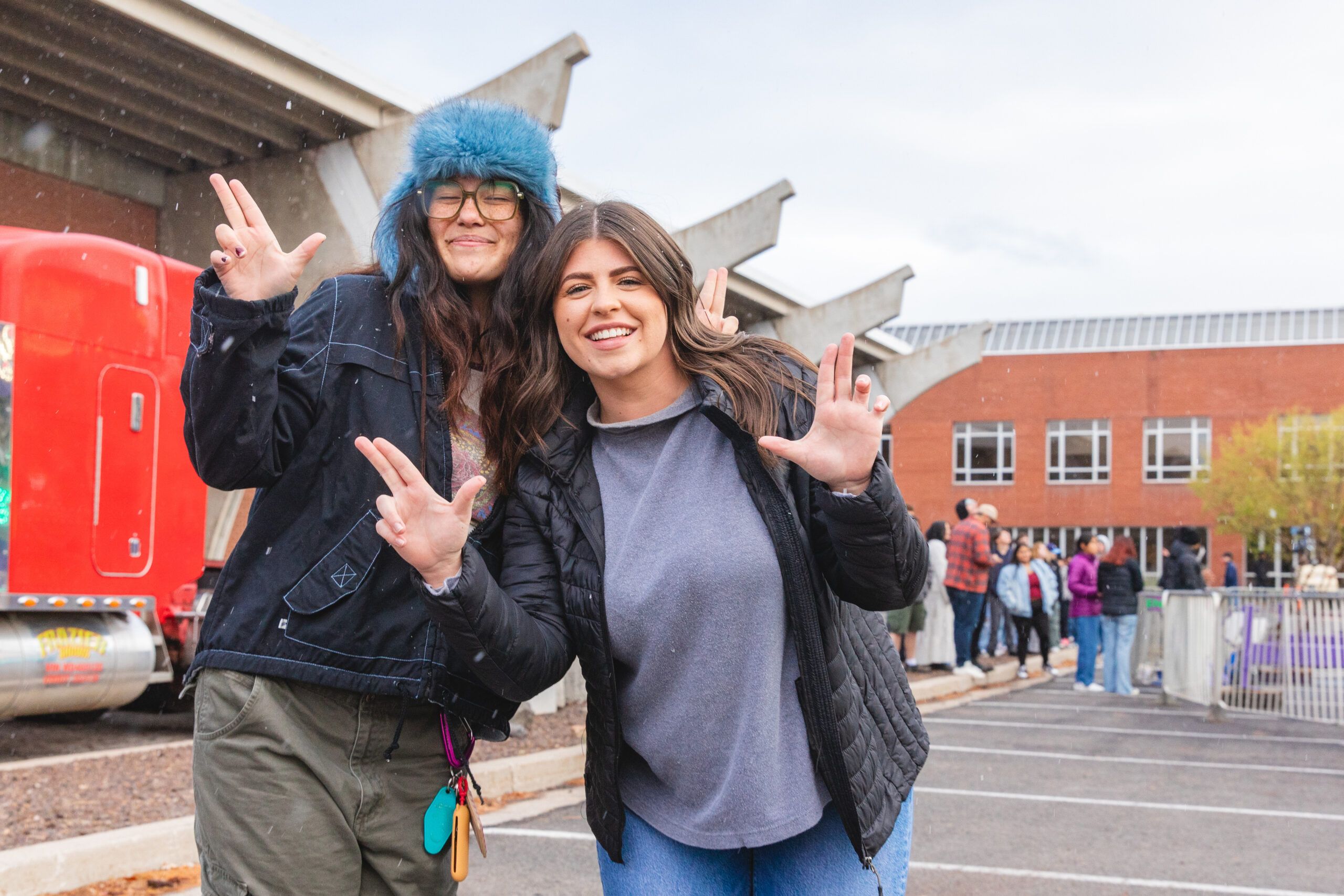 NAU students smile and do the Lumberjack hand symbol on a snowwy day in Flagstaff.