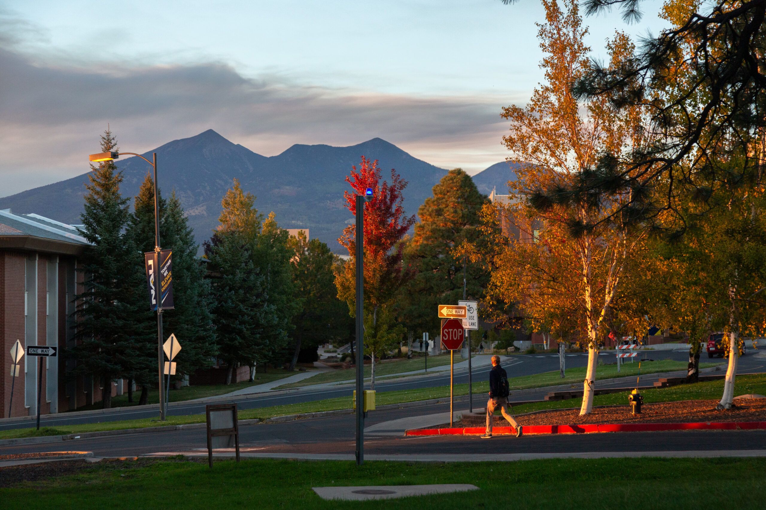 A student walking on the NAU campus, surrounded by beautiful fall tree colors.